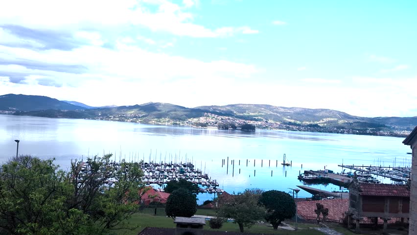 Vigo Estuary, Galicia: A sweeping pan left captures blooming spring trees framing the serene waters and marina, highlighting the picturesque Spanish coastline. Spain.