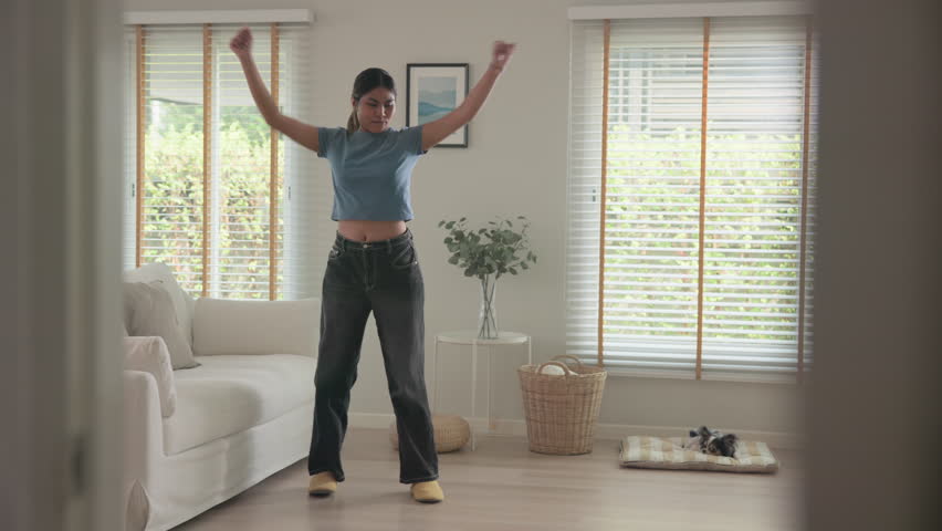 Full length young adult active black asia people Gen Z woman enjoy relax move body happy fun dancer. Humor bizarre music funny dancing crazy joy playful mental at home sofa living room with pet dog.