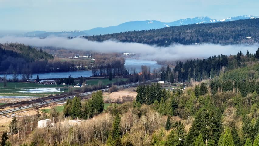 Clouds Over Fraser River And Mountains With Pine Trees In Mission, British Columbia, Canada. - aerial shot