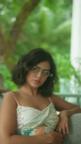A woman in a printed outfit sits thoughtfully on a bench, surrounded by lush greenery in a park