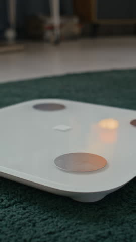 Vertical shot of unrecognizable feet of woman stepping on digital white scale in bedroom