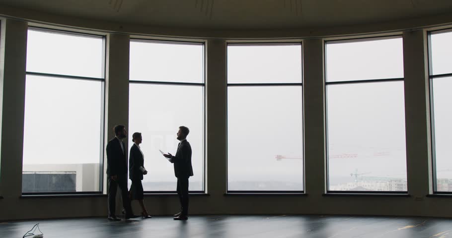 Expert realtor presenting to business professionals spacious office with large panoramic windows. Business people exploring options for purchase or rent in modern space with cityscape in background.
