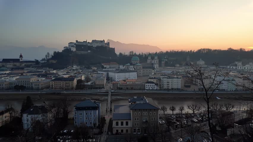 Salzburg, Austria: Panoramic footage of the sunset over Salzburg medieval old town with the famous Fortress Hohensalzburg in winter while a bus ride the road along the river. 