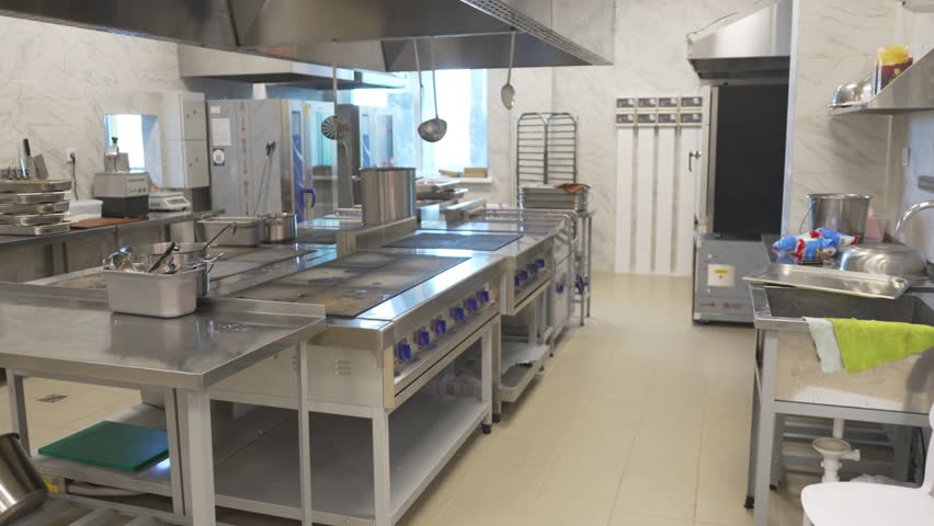 Industrial kitchen features row of cooking stoves and equipment. Hanging ladles and racks add structure to clean renewed workspace
