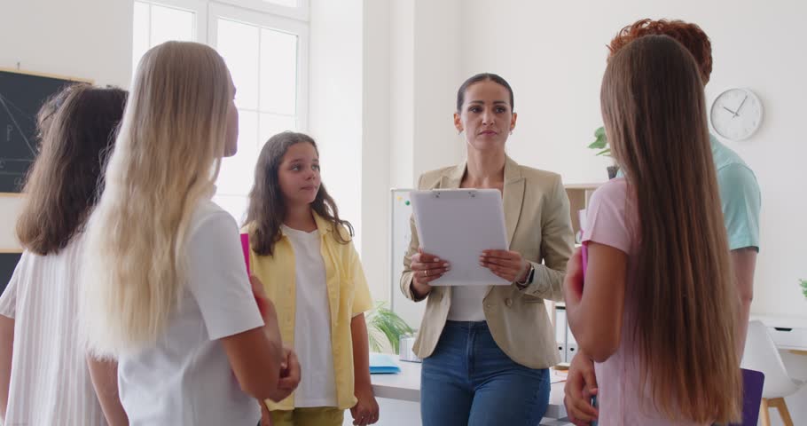 Group of preteen pupils standing in circle with their smiling female teacher, raising hands up and stacking it together. High school children and tutor celebrating success in study and applauding.