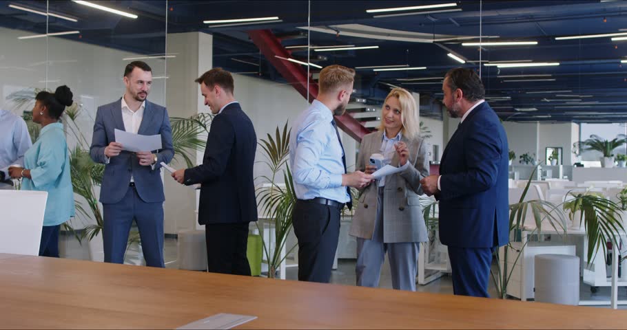 Group of diverse confident business people standing in modern office and talking to each other after a meeting or job conference. Company employees discussing work project . 4k video.