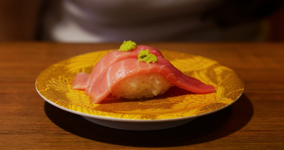 Fatty otoro tuna nigiri sushi resting on golden plate, garnished with small dollops wasabi, showcasing exquisite Japanese culinary craftsmanship in sushi conveyor restaurant