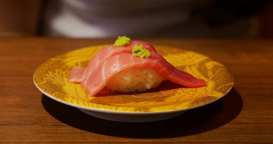 Fatty otoro tuna nigiri sushi resting on golden plate, garnished with small dollops wasabi, showcasing exquisite Japanese culinary craftsmanship in sushi conveyor restaurant