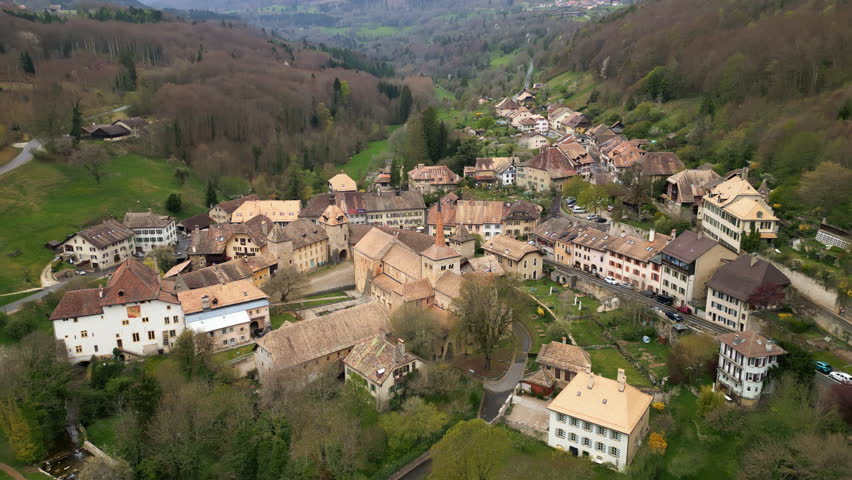 Aerial: Romainmotier Priory, former Cluniac priory, during the day in canton of Vaud, Switzerland, orbit drone shot