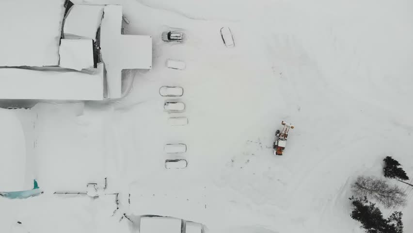 Aerial view of tractor clears snow covered parking lot and roadway for car