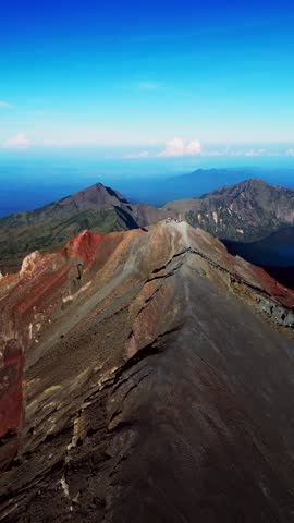 Vertical drone view of Mount Rinjani Summit capturing hikers at the peak surrounded by dramatic volcanic landscapes and stunning morning light from the crater rim of Lombok