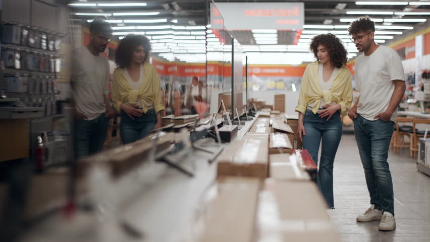 Young couple browsing television display, comparing different models while salesman explaining features in detailed slow motion, highlighting modern electronics shopping experience