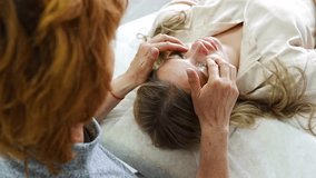 Female practitioner performs facial lifting technique on young woman lying on couch. Concept of energy healing, face therapy and alternative wellness practice from Access Bars. High quality 4k footage - Powered by Shutterstock - Get 15% off with code: PIKWIZARD15