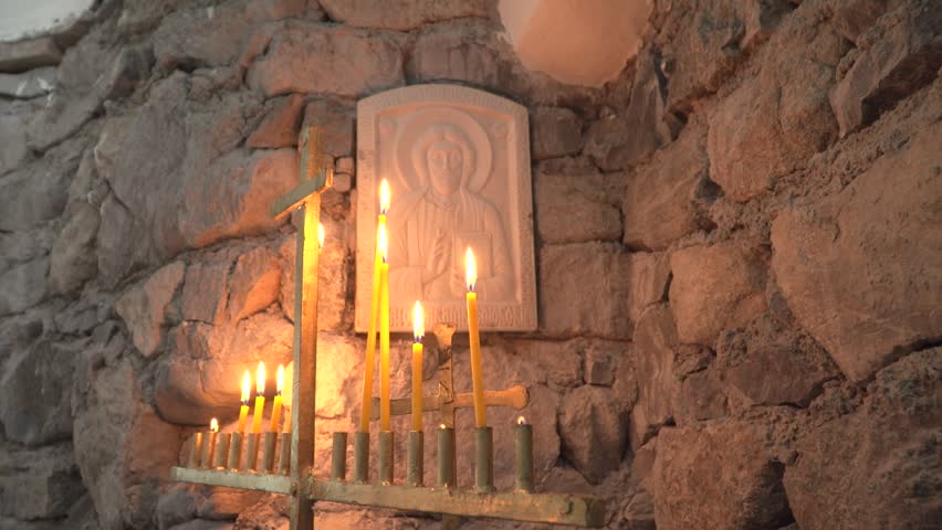 Burning candles in candlestick in front of Orthodox stone icon of Christ. Inside the chapel of St. Nicholas and St. Panteleimon, high in the mountains next to Rai hut. Church made of stone. Masonry.