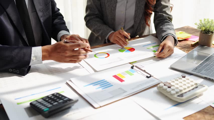 Young colleagues discuss business and analytical price charts using calculators and laptops to calculate financial, tax, accounting, statistics and analytical research ideas.