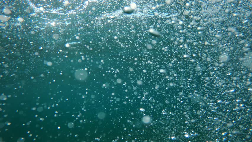 Underwater air bubbles in clean blue ocean water as natural background, low angle view, 4K selective focus