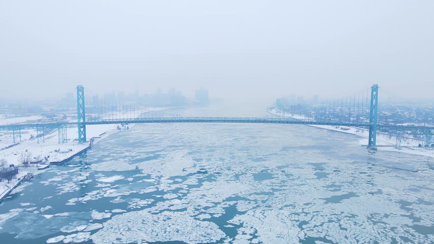 Drone video of Ambassador Bridge stretching across icy Detroit River under overcast winter skies