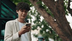 Portrait of young businessman reading message on smartphone with coffee cup on city street. Positive man entrepreneur controls business data via mobile app outdoors. Financial career for students - Powered by Shutterstock - Get 15% off with code: PIKWIZARD15