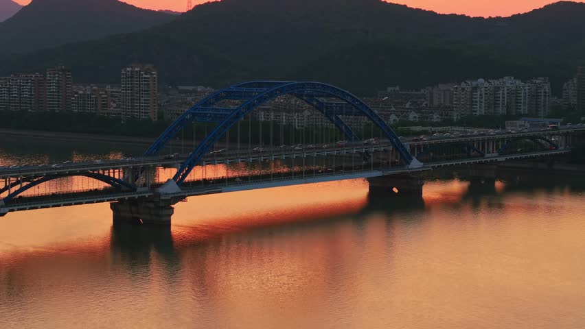 Evening panorama of a blue arch bridge with moving cars over calm water at sunset. Hangzhou, China.