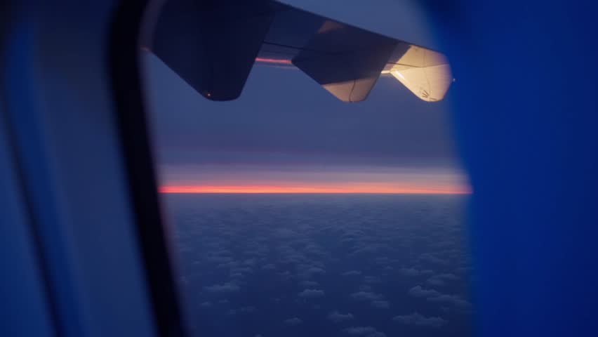 Sunset or sunrise seen from plane window seat during flight with strong colors. Blue clouds and warm red sunny colors in the horizon. Beautiful natural view flying over clouds at dusk or dawn
