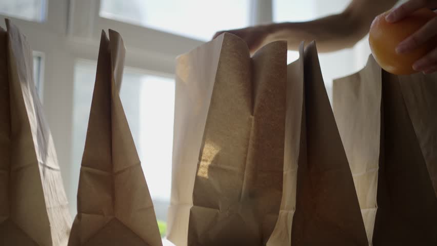 Dedicated volunteer carefully organizing paper lunch bags on table, preparing for upcoming food delivery service supporting local community needs