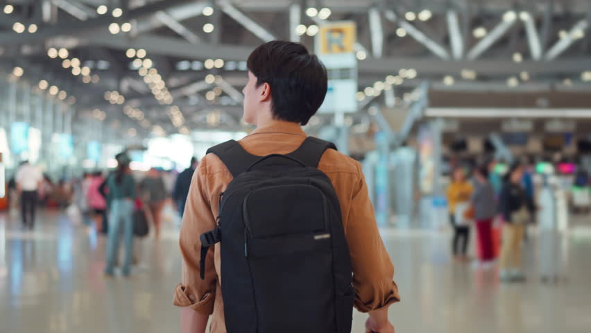 Rear view - Asian man tourist passenger with backpack walking to find his way to the boarding gate inside the airport terminal. Tourist journey concept