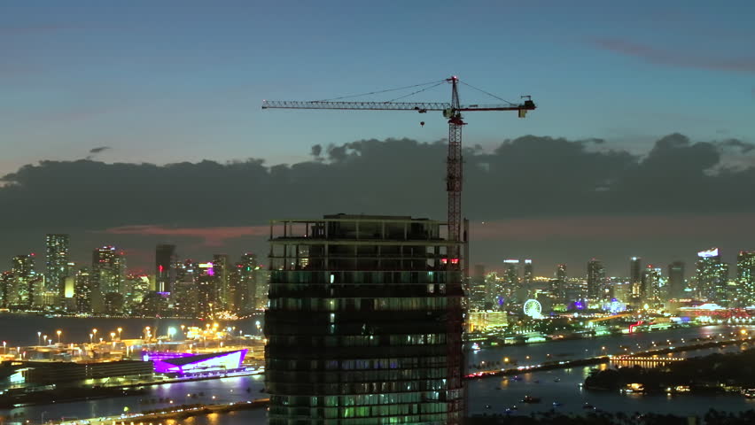 Real estate development in Miami urban area at night. Tower lifting crane at high residential apartment building construction site.