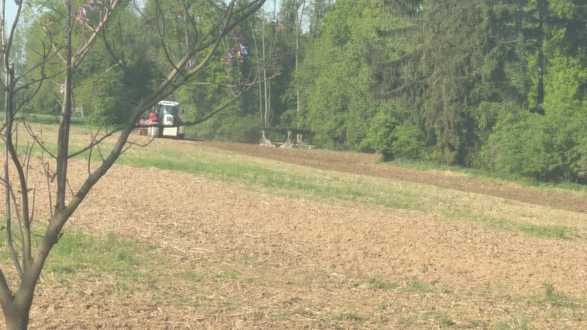 tractor with harrow and seed drill working on agricultural field