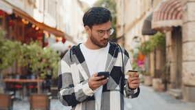 Indian young man using credit bank card smartphone while transferring money, purchases online shopping, order food delivery booking hotel room outdoors. Smiling Hispanic guy on urban city street. - Powered by Shutterstock - Get 15% off with code: PIKWIZARD15