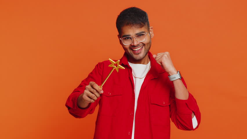 Magician wizard Arabian man gesturing with magic wand fairy stick, making wish come true casting magician spell advertising holidays sale discount. Indian bearded guy isolated on orange background