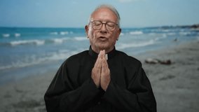 Elderly priest man in black robe praying peacefully on the seaside beach with waves and blue sky, embodying spirituality and serenity outdoors. - Powered by Shutterstock - Get 15% off with code: PIKWIZARD15