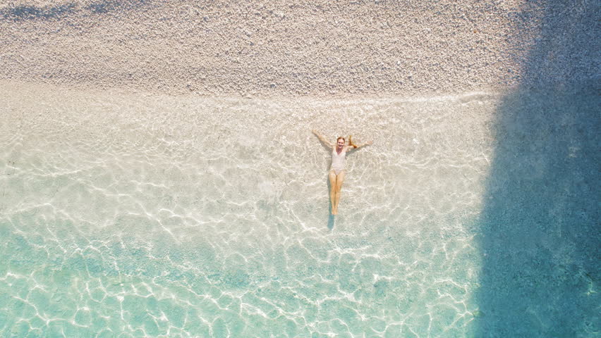 Woman floats in shallow crystal water on white pebble beach in Kefalonia Greece