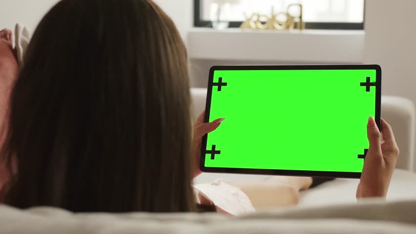 Close-up of woman holding tablet with green screen, orange background behind, suitable for presentations, ads, or chroma key replacement.