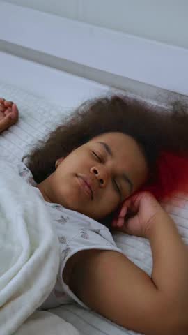 A young person with curly hair enjoys a deep sleep on a comfortable bed, wrapped in soft blankets, as morning light gently illuminates the room.