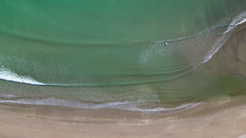 Aerial view looking down on ocean waves meeting the shore on a quiet New Zealand beach.