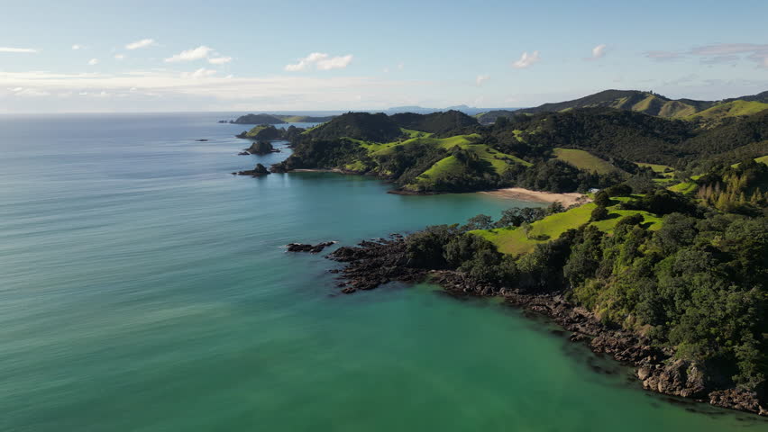Aerial drone view of lush green hills and calm sea meeting the rocky coast near Helena Bay in New Zealand.