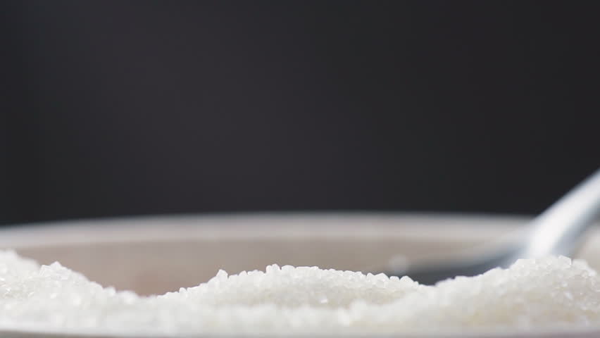 Grains of natural cane sugar are pouring out of a spoon. Macro shot. Product of organic farming. Closeup view of sugar crystals.