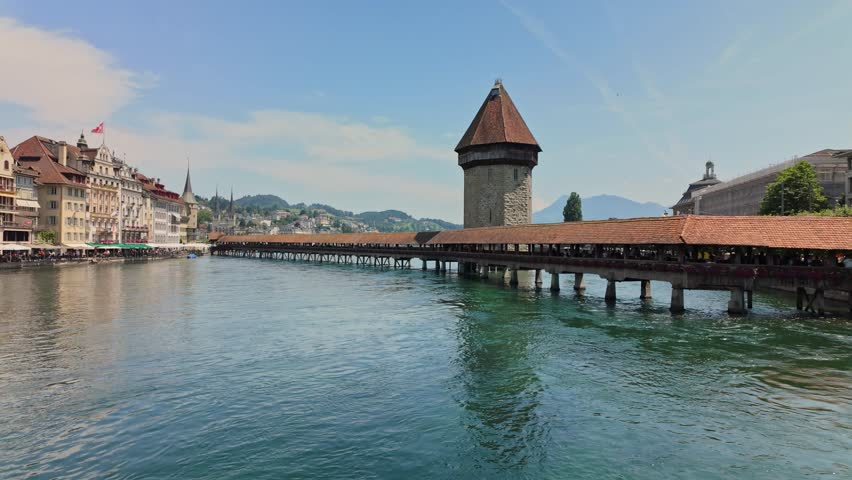 Chapel Bridge in Lucerne, Switzerland, a historic wooden bridge with a tower, spanning the Reuss River. 4K UHD video.