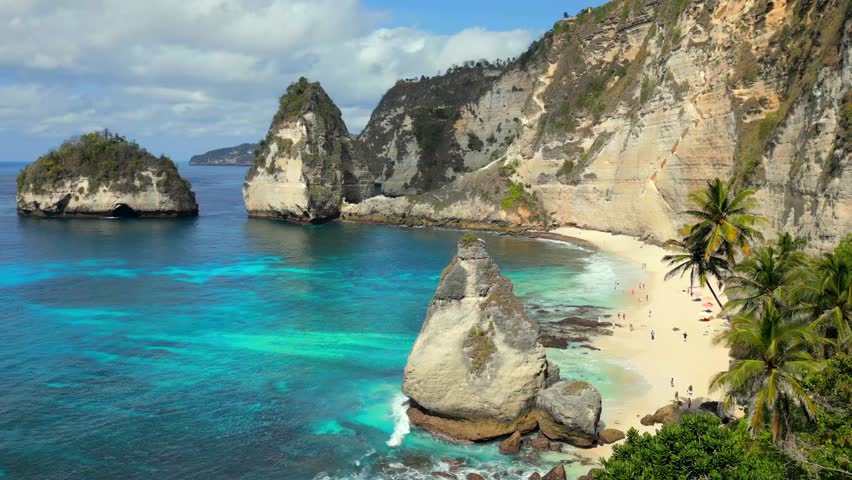 Aerial view of iconic Diamond Beach with limestone cliffs, turquoise ocean, white sand, and palm trees on Nusa Penida Island, Bali, Indonesia.
