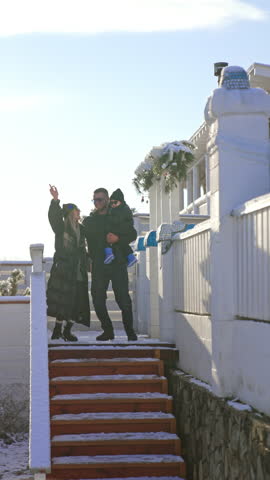 Happy joyful family of three stands outdoors in winter. People dance cheerfully together near the stairs. Vertical video.