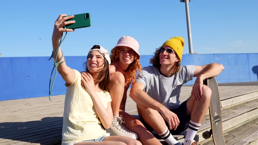 Gen z friends capturing vibrant summer moments, snapping selfies and enjoying skateboarding camaraderie under bright blue skies at urban recreational space