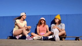 Three friends enjoy a sunny day at the skate park, chatting and relaxing beside their skateboards, showcasing youthful energy and friendship - Powered by Shutterstock - Get 15% off with code: PIKWIZARD15