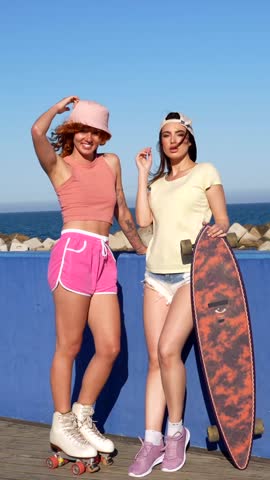 Two friends relax by the ocean, showcasing roller skates and a longboard. Their casual vibe radiates summer fun and leisure by the sea