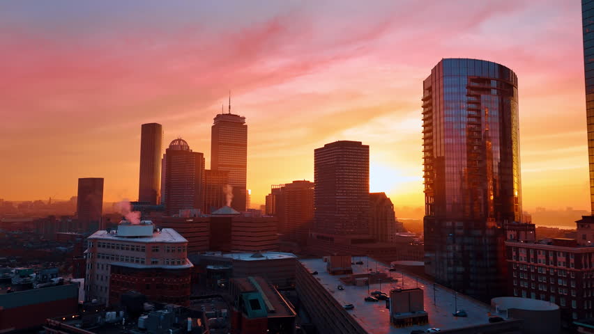 Pink light coloring the scenery of beautiful Boston, Massachusetts, USA. Smoke rises from the pipes of the high-rise buildings. Sunset time city aerial.