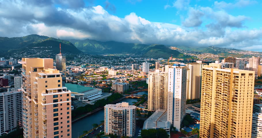 Rising over Waikiki scenery at daytime. Ala Wai Canal separates resort area from Honolulu cityscape. Huge clouds cover the mountain tops at backdrop.