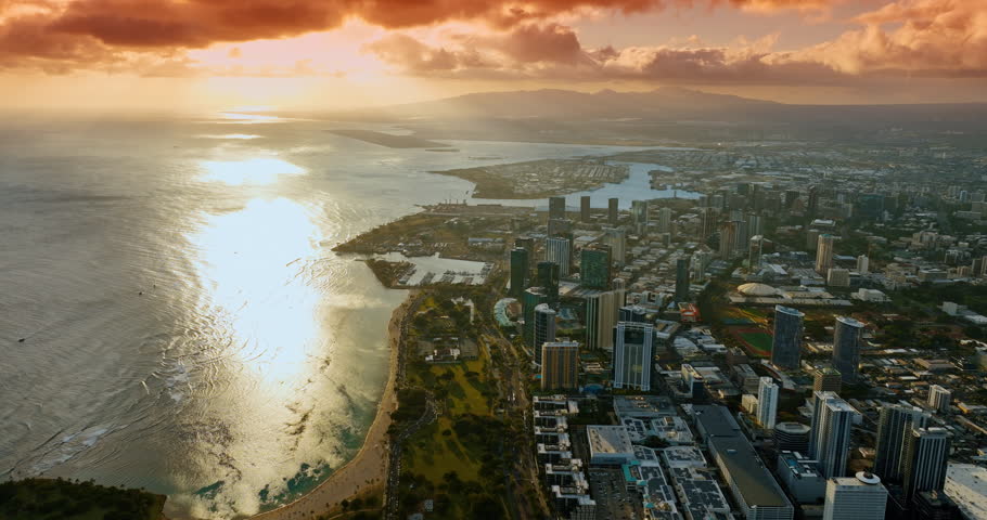 Flying over the green park at the shore of Honolulu, Hawaii, USA. Orange clouds are in the sky. Spectacular view of the coast of the Pacific Ocean at sunset.