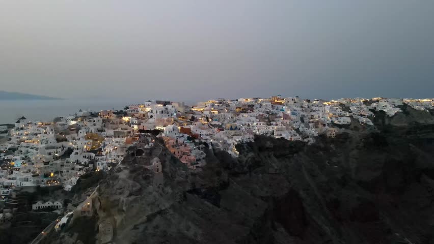 Stunning aerial view of Oia village on Santorini island, Greece, at sunset. The iconic white-washed houses, blue domes, and golden light create a breathtaking and romantic atmosphere.