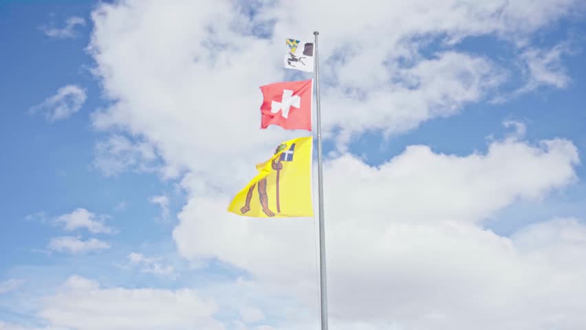 Appenzell innerrhoden and swiss flags waving on a flagpole with clouds and blue sky