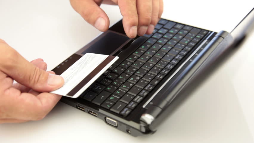 Black laptop on a white table. Men's hands typing information from credit card