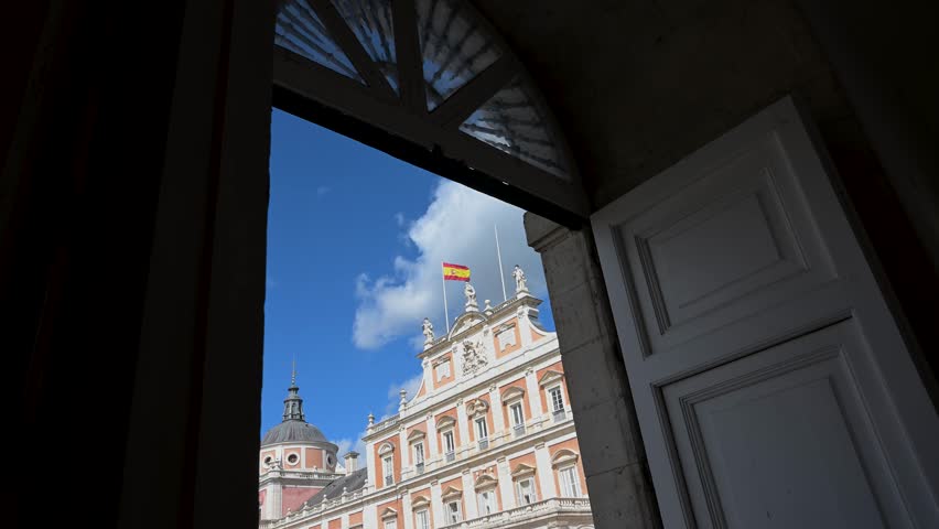 Aranjuez Royal Palace, Spain: On a sunny day, this 18th-century royal residence is viewed through a door, framing its grand architecture—a key tourist landmark reflecting royal heritage.